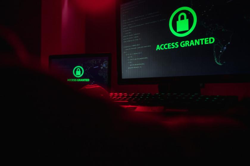 Ein Hacker sitzt vor zwei Bildschirmen mit dem grünen Schriftzug Access Granted.