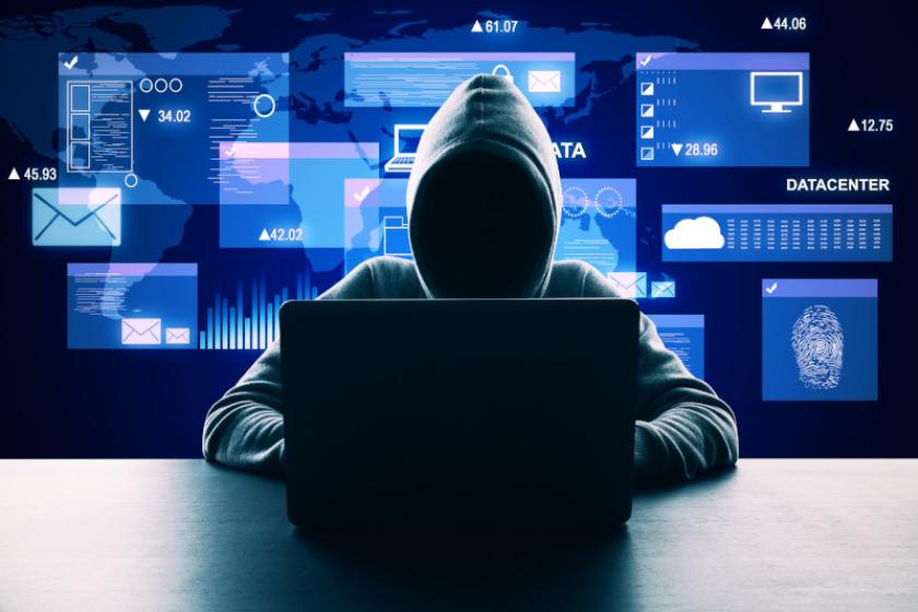 Ein Hacker mit Kapuzenpulli sitzt vor einem Laptop. Im Hintergrund schweben stilisierte Bildschrimfenster.