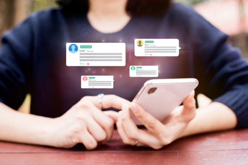 Frau sitzt an einem Tisch und blickt auf ihr Smartphone, über dem Chatblasen schweben.