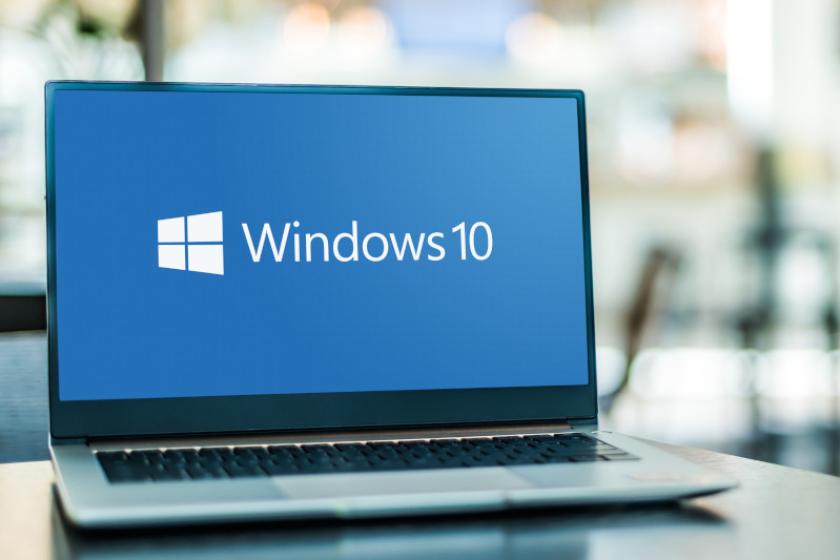 Ein aufgeklappter Laptop steht auf einem Tisch, auf dem Bildschirmt steht auf blauem Hintergrund "Windows 10