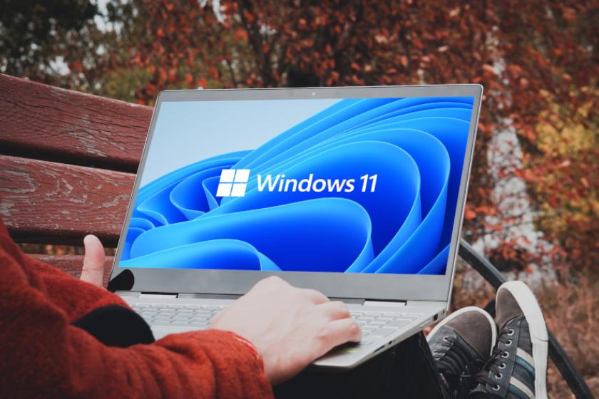 Ein Mann sitzt auf einer Parkbank mit einem Laptop auf dem Schoß. Auf dem Bildschirm steht Windows 11.