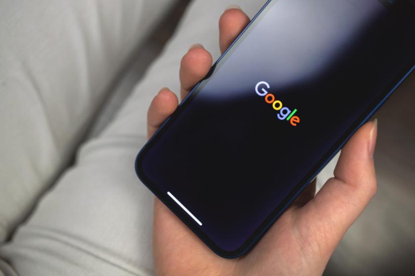 Ein Smartphone mit dem Schriftzug "Google" auf dem Bildschirm liegt in der Hand einer Frau.