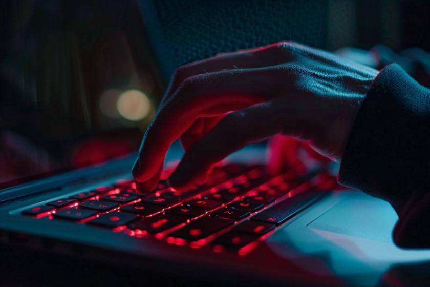 Rot angeleuchtete Hände tippen auf einer Laptoptastatur.