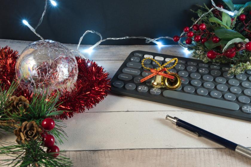 Eine schwarze Tastatur steht auf einem hellen Holztisch, der mit Weihnachtsdekoration geschmückt ist.