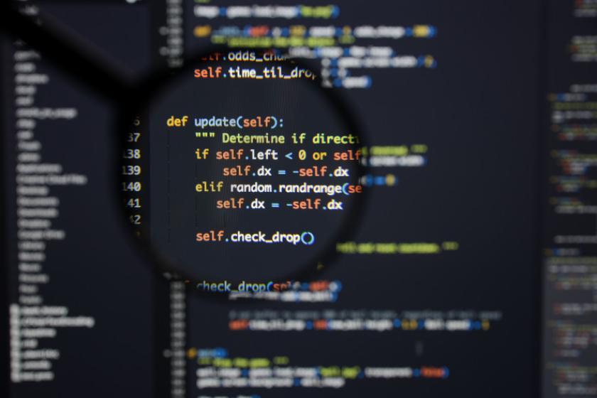 Eine Lupe vergrößert einen Ausschnitt von Programmiercode auf einem Bildschirm.