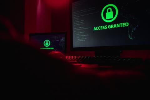 Ein Hacker sitzt vor zwei Bildschirmen mit dem grünen Schriftzug Access Granted.