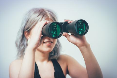Junge Frau schaut durch ein Fernglas.