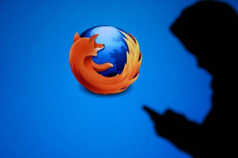 Ein Firefox-Logo auf blauem Hintergrund mit dem Schatten einer Person im Vordergrund, die ein Smartphone hält.
