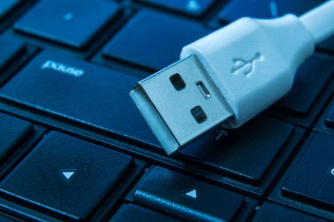 Ein weißer USB-Stecker liegt auf den Tasten einer schwarzen Tastatur.