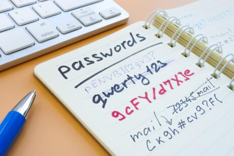 Ein aufgeschlagener Notizblock mit darin notierten Passwörtern liegt vor einer Tastatur.