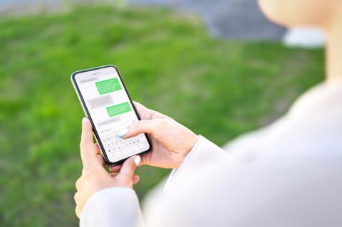 Frau blickt draußen auf einer Wiese auf einen Chatverlauf auf ihrem Smartphone, über die Schulter fotografiert..