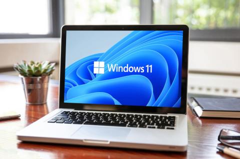 Ein aufgeklappter Laptop steht auf einem Holzschreibtisch mit einem Windows 11-Logo auf dem Bildschirm.