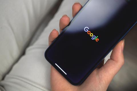 Ein Smartphone mit dem Schriftzug "Google" auf dem Bildschirm liegt in der Hand einer Frau.