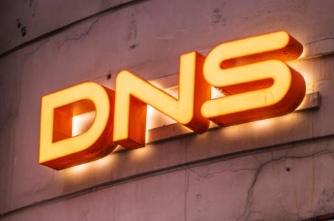 Orangefarbene Leuchtbuchstaben an einer Betonwand bilden den Schriftzug DNS.