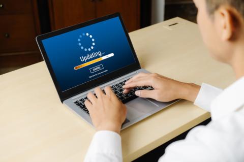 Geschäftsmann sitz an seinem Laptop, auf dessen Bildschirm ein Update-Hinweis steht.