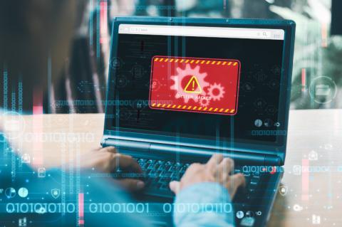 Mann sitzt vor einem Laptop mit der roten Warnmeldung auf dem Bildschirm "System Hacked".