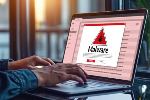 Zwei Hände tippen auf der Tastatur eines Laptops, auf dessen Bildschirm ein rotes Warndreieck mit einer Malware-Warnung darunter erscheint.