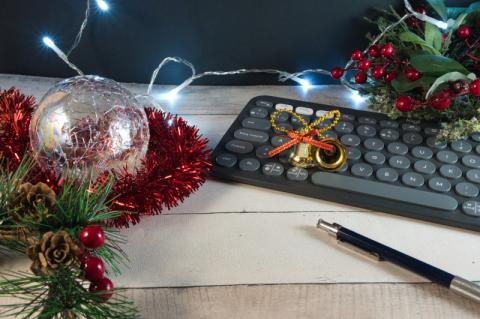 Eine schwarze Tastatur steht auf einem hellen Holztisch, der mit Weihnachtsdekoration geschmückt ist.