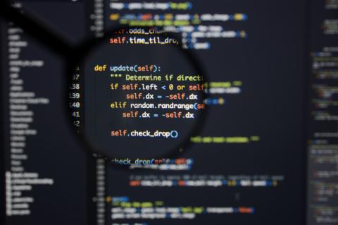 Eine Lupe vergrößert einen Ausschnitt von Programmiercode auf einem Bildschirm.