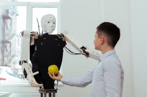 Junge hält einem Roboter einen grünen Apfel hin