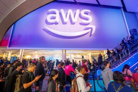 Besucher der AWS re:Invent 2025 bewegen sich in der Veranstaltungshalle. An einer Wand hängt ein großes, weißes AWS-Logo.