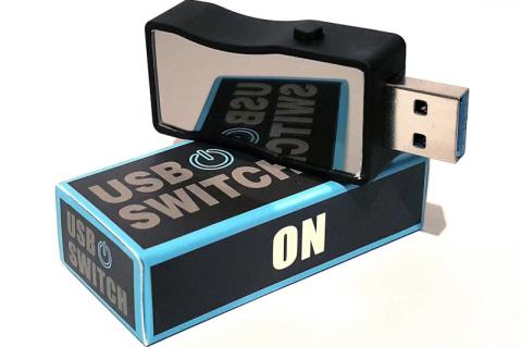 Ein USB-Schalter mit kleinem Knopf an der Seite liegt auf einer zugehörigen Verpackung.